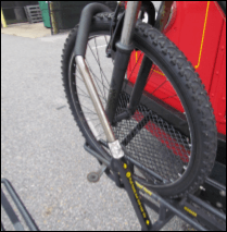 A bicycle with it's tire secured in a bus bike rack by the support arm of the rack